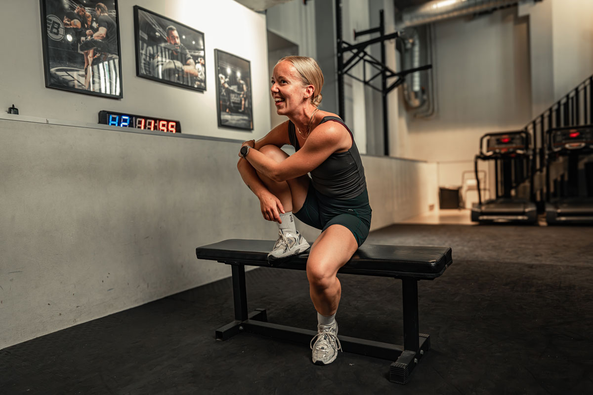 Coachen smiler i et fitnesscenter ved en vægtstang.